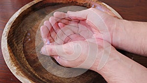 Man puts his hands in a wooden bowl of water and grabs the water in his fists