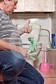A man puts on household rubber gloves to wash a dirty toilet
