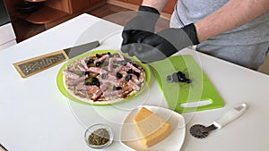 A man puts olives on a pizza base. Cooking ingredients are laid out nearby. Making pizza at home