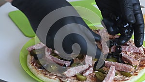 A man puts olives on a pizza base. Cooking ingredients are laid out nearby. Making pizza at home. Close-up shot