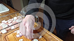 A man puts onion slices on chicken tenders. Putting onion rings on sliced chicken steaks. A hungry dog in the background