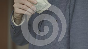 A man puts a pack of dollars in his jacket pocket. close-up video.