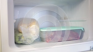 A man puts plastic containers in the fridge. Frozen fruits, vegetables, meat in the freezer.