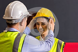 Man puts a safety helmet on woman at factory or plant site. Business heir concept. Happy lover wearing safety helmet on together