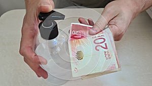 Man puts sanitizer gel from a bottle on paper israeli money