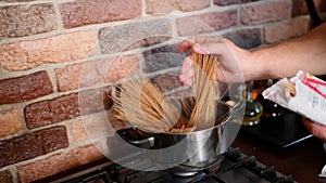 Man puts spaghetti into a pot of boiling water in the kitchen, taking it out of the package, close-up