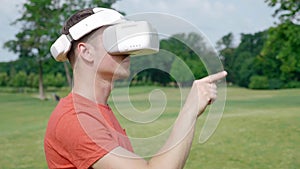 A man puts a VR headset on his head in a park and starts using, then he takes off it