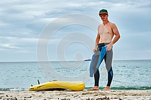 A man puts on a wetsuit on the beach and is going for a walk on the sea on a SUP board. Active recreation.
