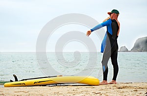 A man puts on a wetsuit on the beach and is going for a walk on the sea on a SUP board. Active recreation.