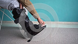 Man putting on ankle brace, Orthopedic ankle support shoes. Injuried guy on chair with Splint, walker boot, Orthosis