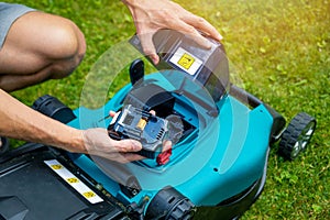 Man putting battery into electric cordless lawn mower