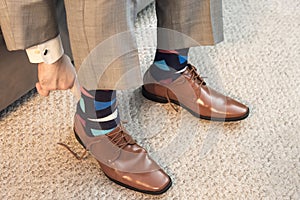 Man putting on brown dress shoes in formal wear with colorful socks