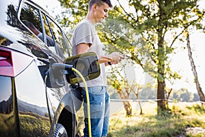 Man putting a charger in a car and adjusting an EV charging app on smartphone