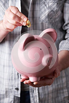 Man Putting Coin Into Large Piggy Bank