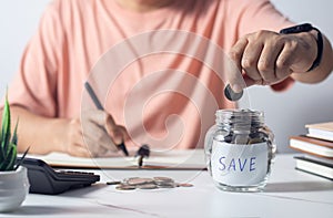 man putting coin in piggy bank and press the calculator with coins placed on the account book money saving concept