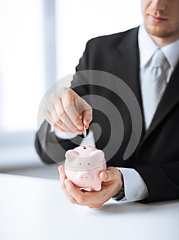 Man putting coin into small piggy bank