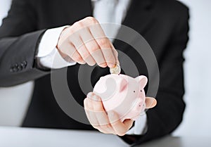 Man putting coin into small piggy bank
