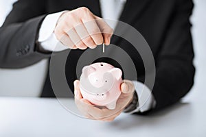 Man putting coin into small piggy bank