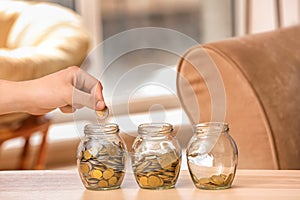 Man putting coins into glass jars on table. Savings concept