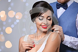 Man putting elegant jewelry on beautiful woman against blurred background