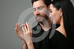 Man putting elegant ring on woman's finger against dark grey background, closeup