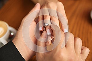 Man putting engagement ring on his girlfriend`s finger in cafe, closeup