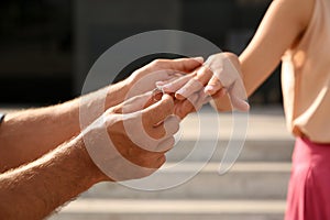 Man putting engagement ring on his girlfriend`s finger outdoors, closeup