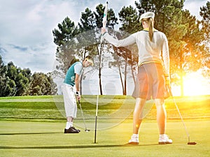 Man putting on green while female golfer holding the pin