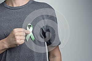 Man putting green ribbon on his shirt. Awareness symbol