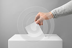 Man putting his vote into ballot box on light background