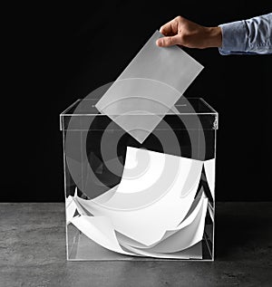 Man putting his vote into ballot box on table against black background