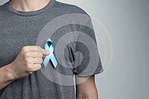 Man putting light blue ribbon on his shirt. Awareness symbol