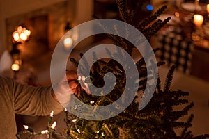 Man putting lights on the Christmas tree in a candlelit home