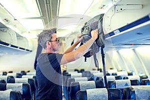 Man putting luggage on the top shelf on airplane