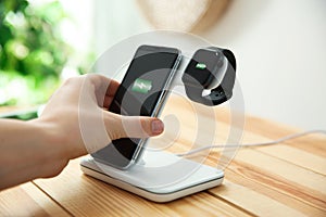 Man putting mobile phone onto wireless charger at table, closeup. Modern workplace accessory