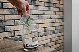 Man putting money into donation jar on table, closeup.