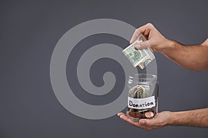 Man putting money into jar with label DONATION on grey background, closeup.