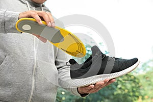 Man putting orthopedic insole into shoe indoors, closeup. Foot care