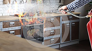 Man putting out burning stove and oven with fire extinguisher in kitchen, closeup