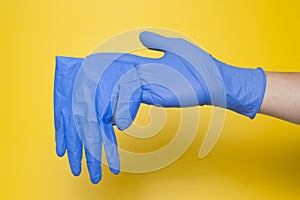 Man putting on a pair of latex gloves on yellow background