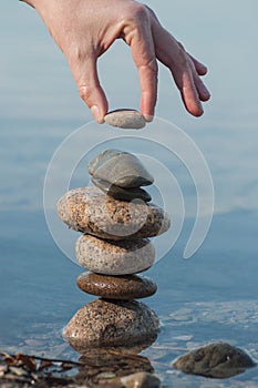 Man putting pebble on stone balance in the water of lake with reflection