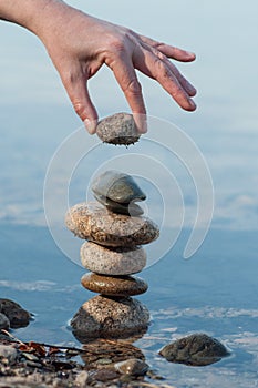 Man putting pebble on stone balance in the water of lake with reflection