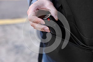 Man putting pepper spray into backpack outdoors, closeup. Space for text