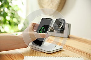 Man putting phone onto wireless charger at wooden table, closeup. Modern workplace accessory