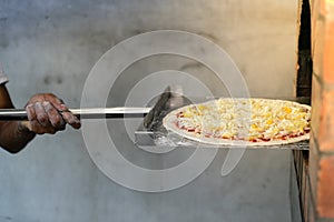 Man putting pizza baking sheet in oven at restaurant kitchen.