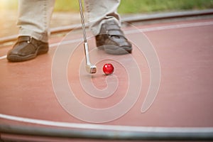 Man is putting a red golf ball with his iron racket