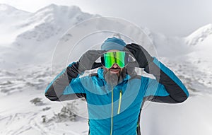 Man putting on ski glasses, preparing for winter skiing in snowy mountains.