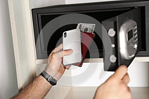 Man putting smartphone, passport and money into steel safe, closeup