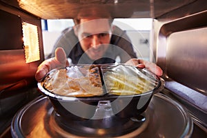 Man Putting TV Dinner Into Microwave Oven To Cook photo