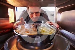 Man Putting TV Dinner Into Microwave Oven To Cook